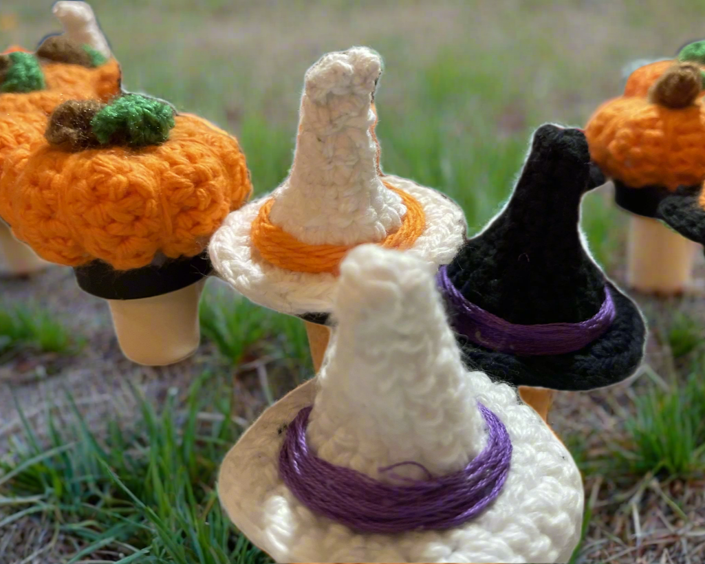 Crocheted pumpkins and witch hats on corks, in a field of grass.