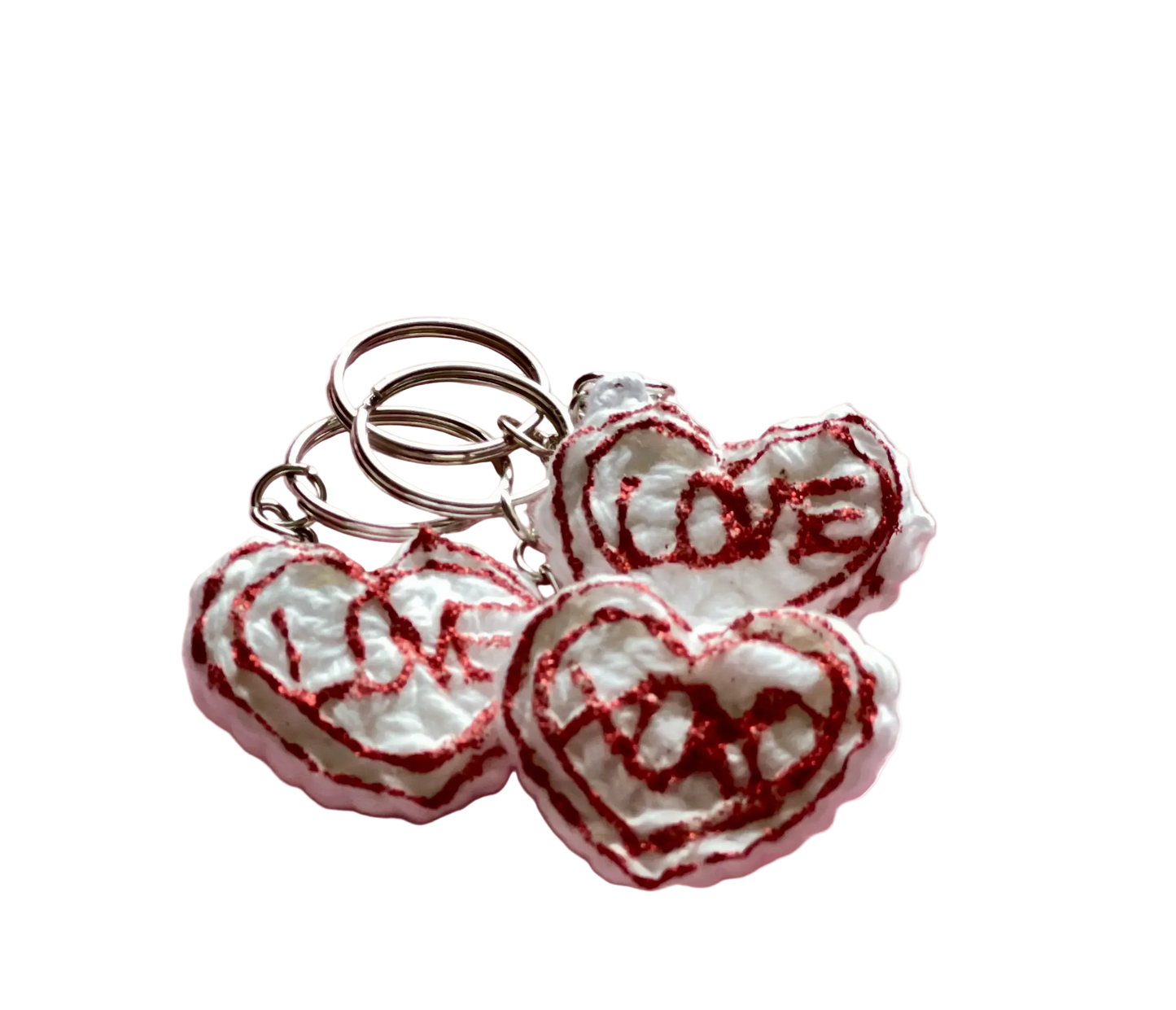 Crocheted white hearts with red lettering reading "love" and "xoxo" attached to keychain rings