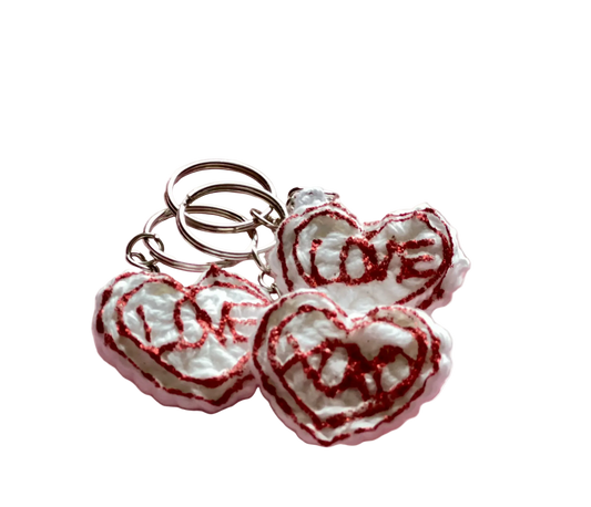 Crocheted white hearts with red lettering reading "love" and "xoxo" attached to keychain rings