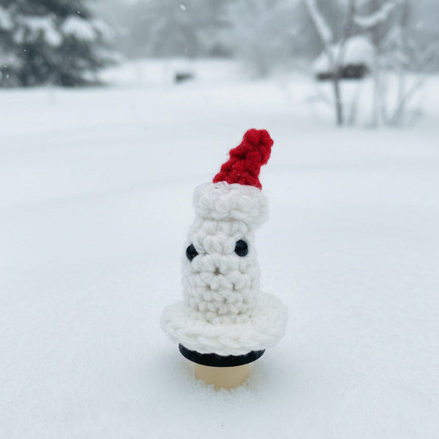 Crocheted ghost on a bottle stopper wearing a red Santa hat in a snowy landscape