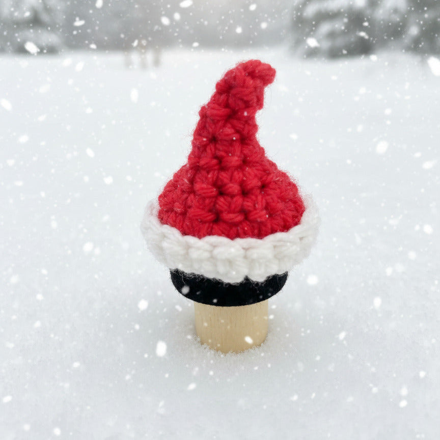 Crocheted Santa hat on a bottle stopper against a snowy backdrop