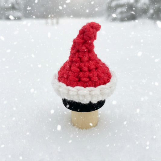 Crocheted Santa hat on a bottle stopper against a snowy backdrop