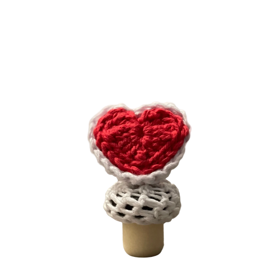 A red crocheted heart with white lace on a bottle stopper