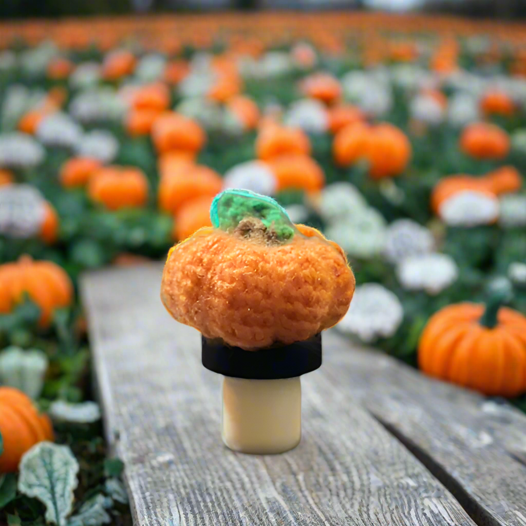 Crocheted pumpkin bottle stopper on a wooden surface with pumpkins in the background