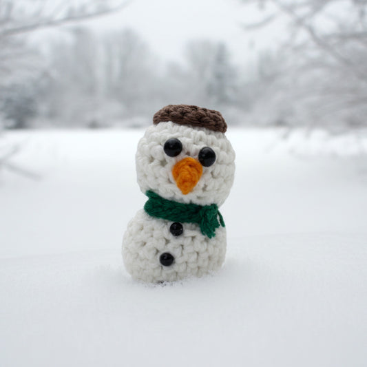 A small crocheted snowman figure with a brown hat and a green scarf