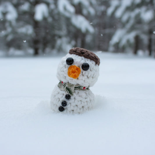 A small crocheted snowman figure with a brown hat and a gray scarf patterned with trees and red dots
