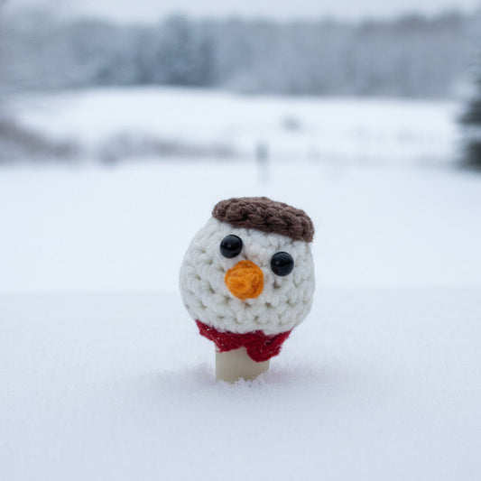 A small crocheted snowman head with a brown hat and a red scarf on a bottle stopper