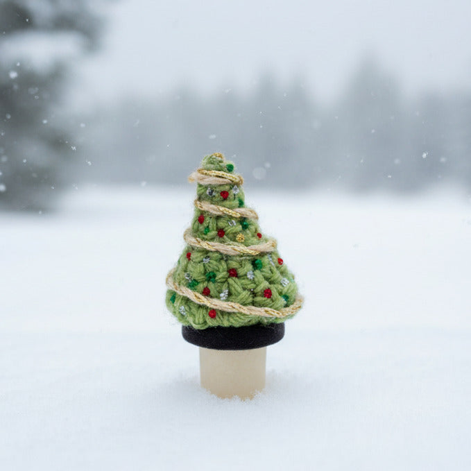 Small crocheted Christmas tree with glittery ornaments and a gold ribbon on a bottle stopper