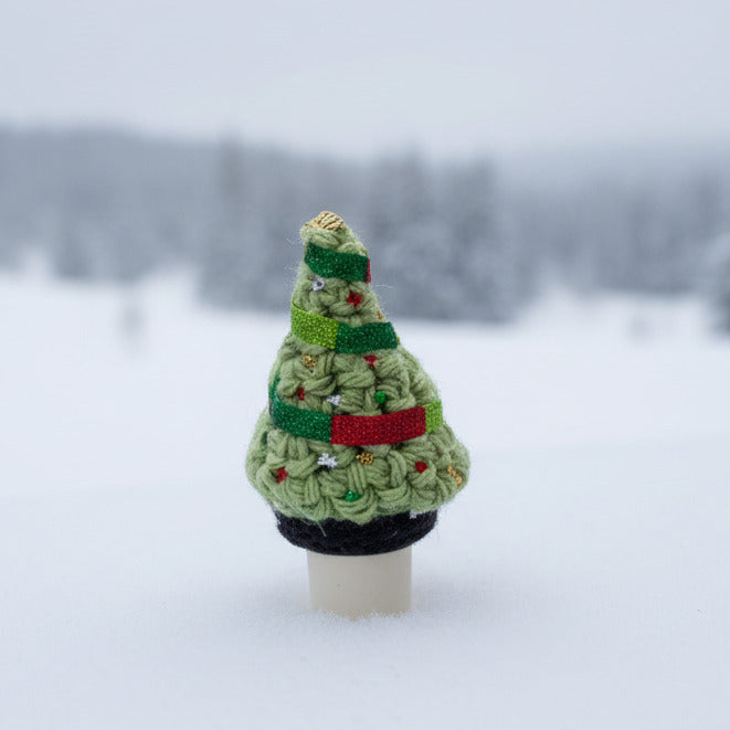 Small crocheted Christmas tree with glittery ornaments and a red and green ribbon on a bottle stopper