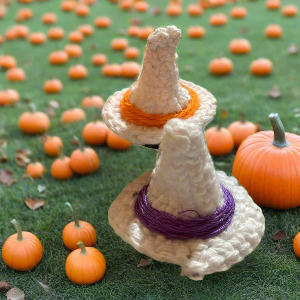 Crocheted witch hat with orange and purple bands on a grassy background with pumpkins.