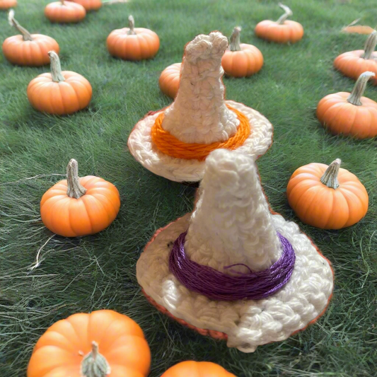 Crocheted witch hats with colorful bands on a grassy background with pumpkins.